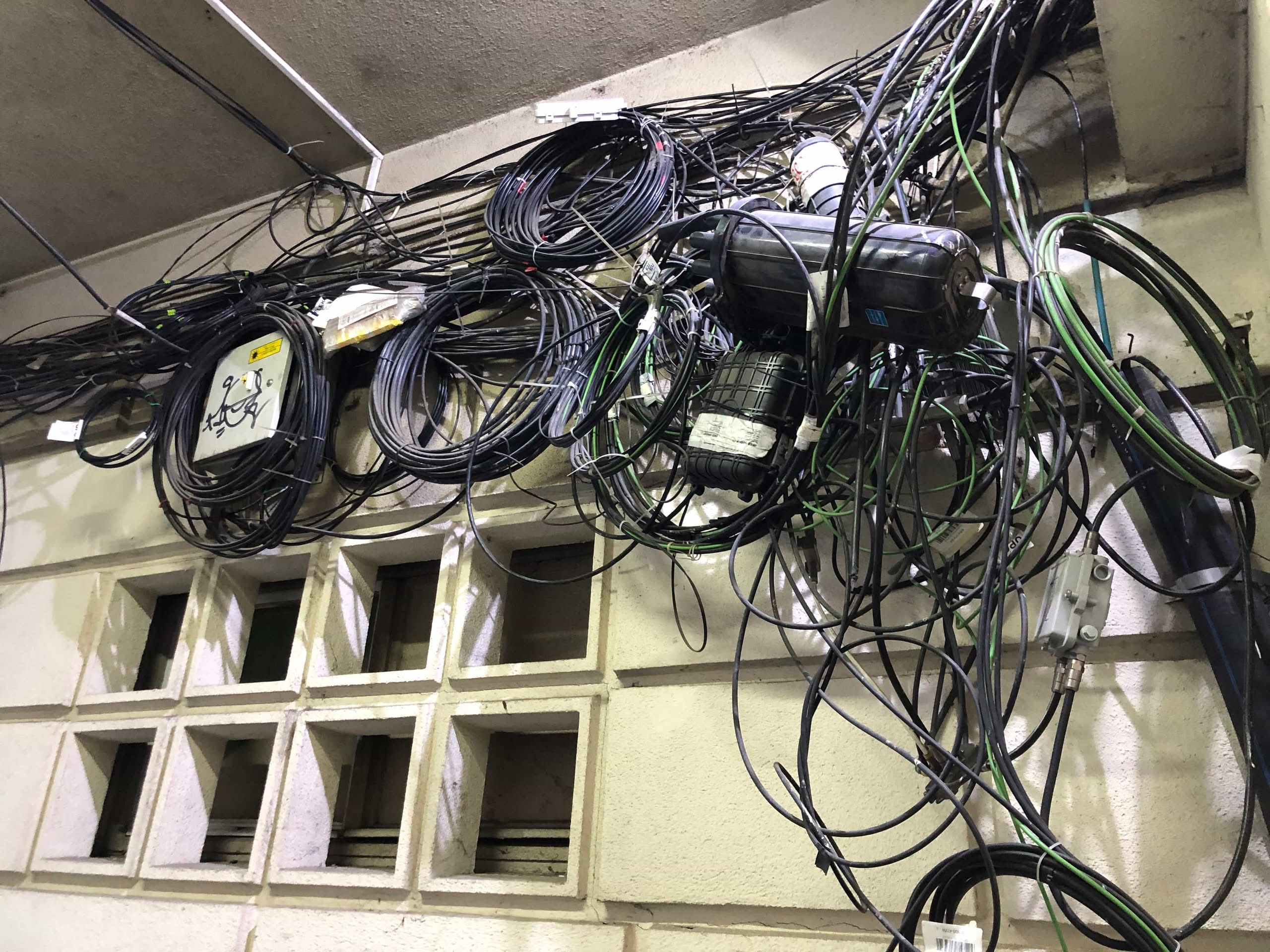 Overloaded Breakers: Why Your AC Trips the Fuse Box (Fix) 1 A chaotic, tangled mess of overlapping lines on a building wall, illustrating the severe clutter and safety hazards associated with unmanaged wiring and overloaded breakers in Dallas, Texas.
